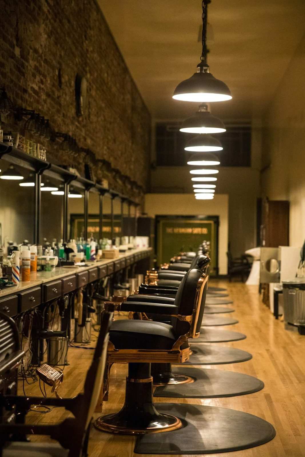 Fila de sillones de barbería con lámparas colgantes a lo largo del local